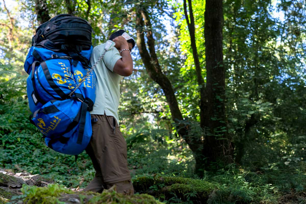 Porter carrying Footprint Adventure's duffle bag through forested Annapurna trail